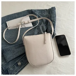 Detail showing creamy white pebble grain texture and adjustable strap on a U-shaped bag