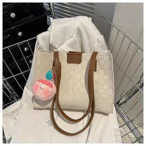 Close-up of cream tote bag with checkered texture, brown strap and pink peach pendant