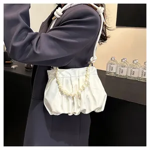Detail of white pleated cloud bag featuring a large pearl handle and braided strap