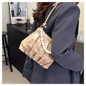 Detail of beige pleated shoulder bag with oversized pearl strap and gold hardware accents