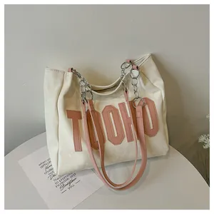 Detail of cream tote bag with pink letter embroidery and silver chain shoulder strap