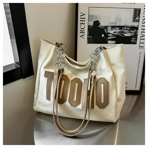 Detail of white leather tote bag with brown letter applique and metal chain strap