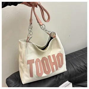 Detail of the pink leather handle and silver chain on the large beige tote bag