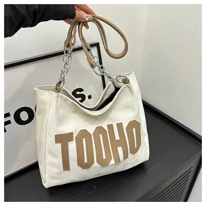 Macro detail of large cream tote bag with brown TOOHO lettering and chain strap
