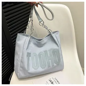 Macro detail of large tote bag showing silver chain handles and TOOHO logo patch