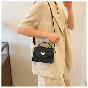 Détail du sac à main noir pailleté avec breloque papillon blanc sur veste beige