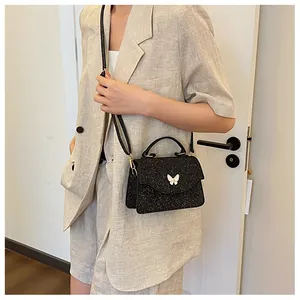 Détail du sac à bandoulière noir pailleté avec ornement papillon blanc sur le rabat avant