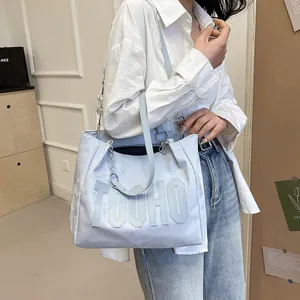 Light blue contrast letter tote bag with metal chain strap worn by a model in daylight