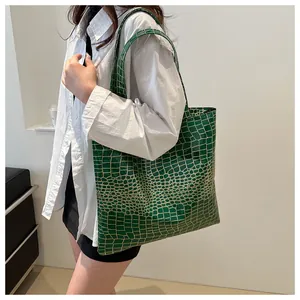 Detail of dark green crocodile texture tote bag with glossy finish and long shoulder straps