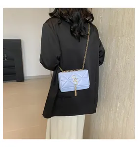 Detail of light blue crossbody bag with gold chain strap and metal tassel on black blazer