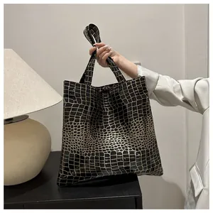 Detail of glossy black crocodile embossed tote bag with large capacity and long handles