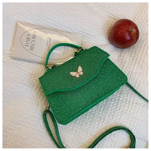 Détail du sac à bandoulière vert à paillettes avec un charmant papillon blanc décoratif