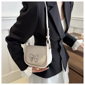 Détail d'un sac besace en cuir crème orné d'un nœud décoratif en métal argenté brillant