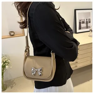 Sacoche beige avec nœud argenté porté en bandoulière pour un style chic et moderne