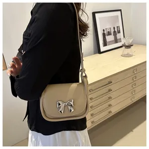 Gros plan d'un sac selle crème avec nœud en métal argenté et texture de cuir délicat