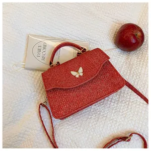 Détail du sac à bandoulière rouge pailleté avec charm papillon blanc et sangle