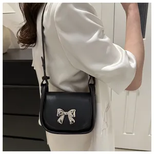 Détail d'un mini sac à bandoulière noir avec un nœud en métal argenté et cuir texturé