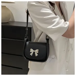 Détail d'un sac selle noir avec nœud argenté porté par un mannequin en costume chic