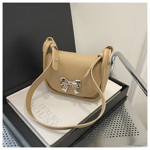 Détail du sac selle beige avec boucle décorative en nœud argenté et texture de cuir fin
