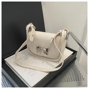 Détail d'un sac selle blanc crème avec un nœud en métal argenté et une bandoulière nouée