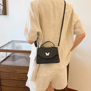 Petit sac carré noir brillant avec papillon blanc porté par un mannequin