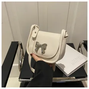 Gros plan du sac besace en similicuir crème avec un détail chic de nœud métallique