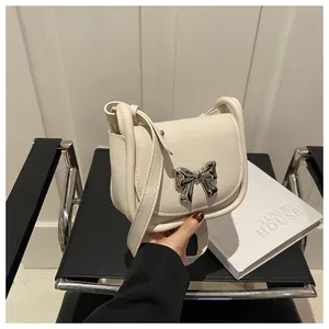 Détail d'un petit sac bandoulière crème avec un grand nœud en métal argenté élégant