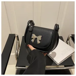 Détail du mini sac selle noir avec nœud métallique argenté et texture en cuir