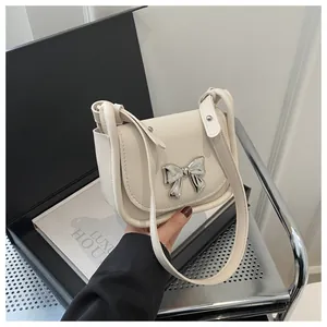 Détail d'un mini sac selle blanc crème avec un nœud en métal argenté et bandoulière cuir