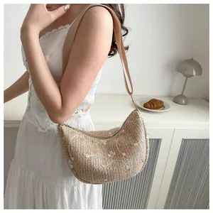 Detailed close-up of woven crescent bag with floral embroidery and wide fabric strap