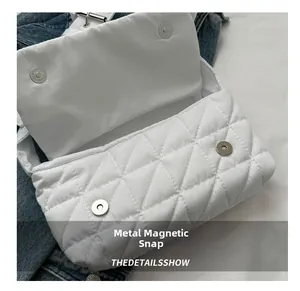 Detail shot of the magnetic metal buckle on a white quilted crossbody nylon bag