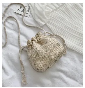 Detail der beigen Stroh-Beuteltasche mit rosa Blütenstickerei und gewebtem Seilgurt