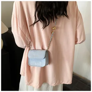 Detail of light blue mini square crossbody bag with gold chain and metal bead on a model