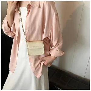 Detail of a creamy white mini square flap bag with gold chain strap on a model