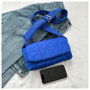 Detail of blue quilted crossbody bag with adjustable wide strap on denim fabric