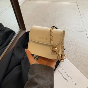 Minimalist cream mini square chain bag with golden rich rabbit text and metal ball