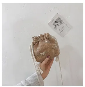 Détail d'un sac seau en paille tissée avec dentelle florale et cordon de serrage à pompon