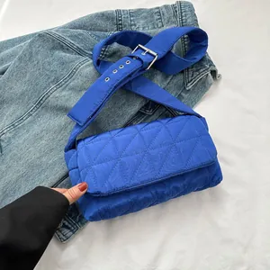 Detail of bright blue quilted crossbody bag with wide adjustable strap on denim background