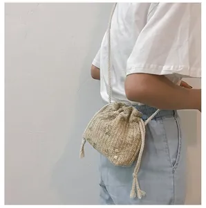 Détail du sac seau en paille avec broderie florale, cordon de serrage et pompons
