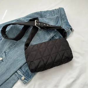 Detail of black quilted crossbody bag with wide adjustable strap on denim background