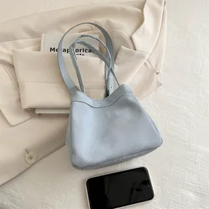Sac seau bleu clair minimaliste avec double poignée posé sur une veste de blazer beige