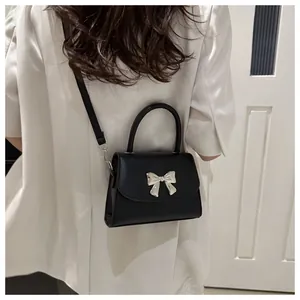Detailed view of black leather mini crossbody bag with silver bow accent on a model
