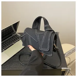 Détail du sac bandoulière en toile noire avec surpiqûres blanches et rabat asymétrique