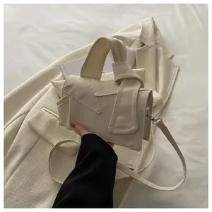 Détail du sac bandoulière en toile crème avec poignée nouée et rabat asymétrique