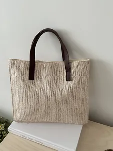 Detail of herringbone weave straw tote bag with brown leather handles on neutral background