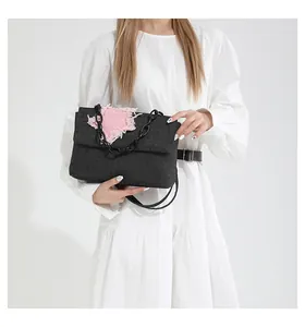 Detail of black denim shoulder bag with pink frayed heart patch and chunky chain strap