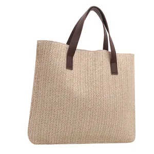 Detailed view of woven straw tote bag with intricate V-pattern and brown leather handles