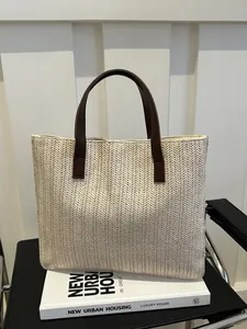 Detail of herringbone weave texture and brown leather handle on straw tote bag
