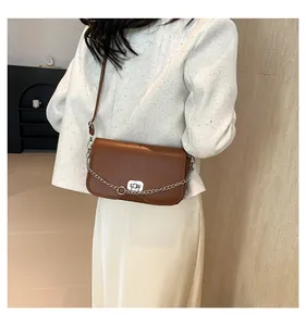 Détail d'un sac bandoulière en cuir marron avec chaîne argentée et boucle de fermeture métal