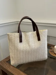 Close-up of woven straw tote bag featuring herringbone texture and brown leather handles